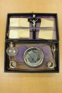 Sick call box opened to show purple lining, crucifix, two candle holders, glass holy water bottle, white linen cloth, and spoon
