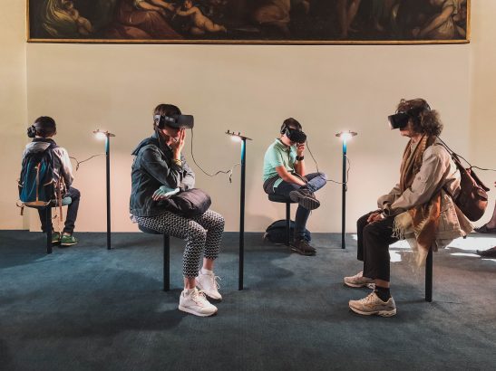 4 individuals seating in a room with Virtual reality headsets on