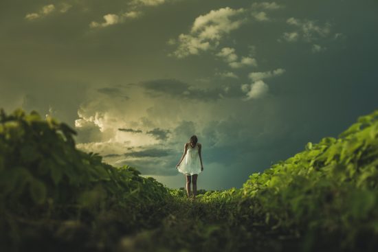 a girl walking alone on the hills with a dark clouds and a bit of sun