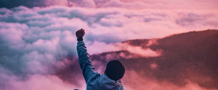 Boy on top of a mountain raising arm in victory