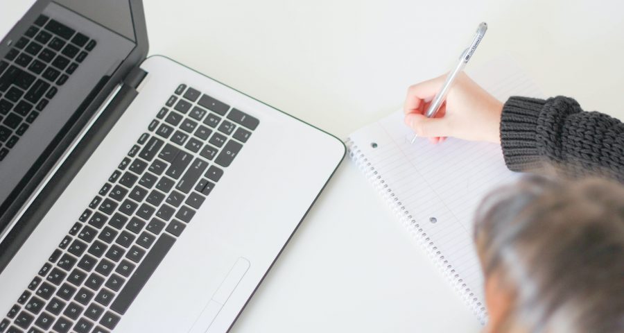 A woman writing on a note next to a laptop