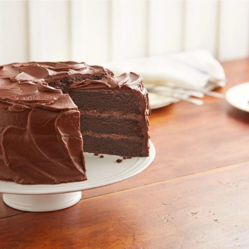 chocolate cake on a cake stand with a slice on a plate next to it