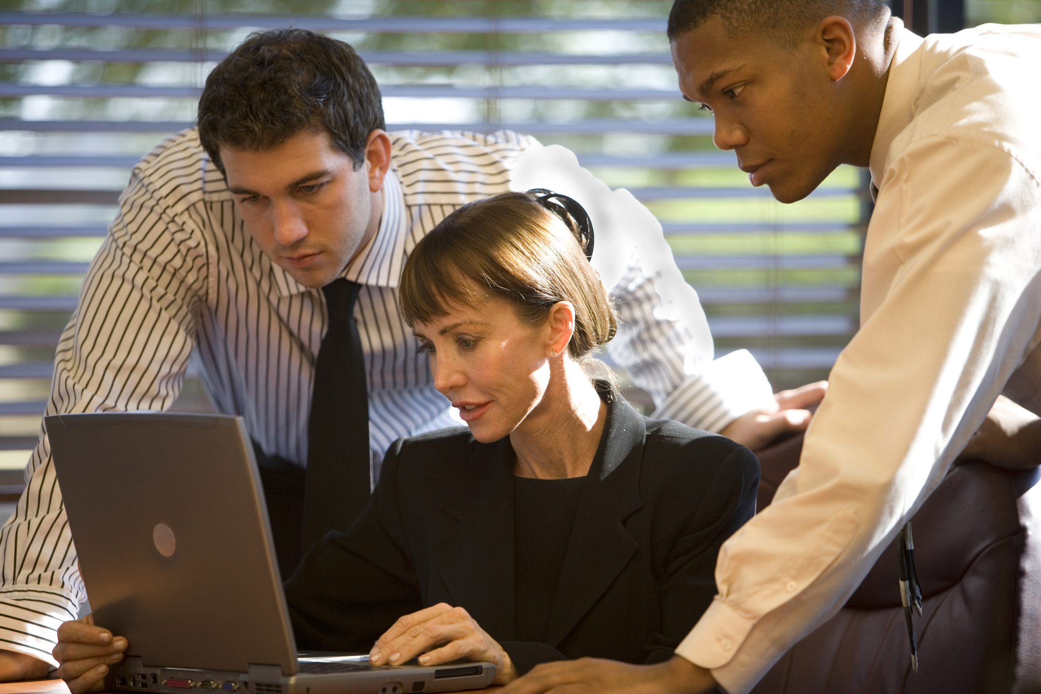 A photo of three businesspeople working together in front of a laptop computer.