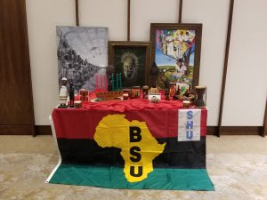 A table with the red, black, and green stripes, a yellow outline of Africa and the initials BSU with Kwanzaa artwork on top of the table