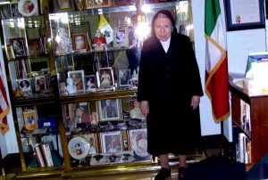 Religious sister in nun's habit standing next to shelf of memorabilia of Pope Pius XII