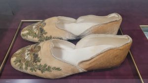 pair of ornate velvet slippers, tan with green floral embroidery